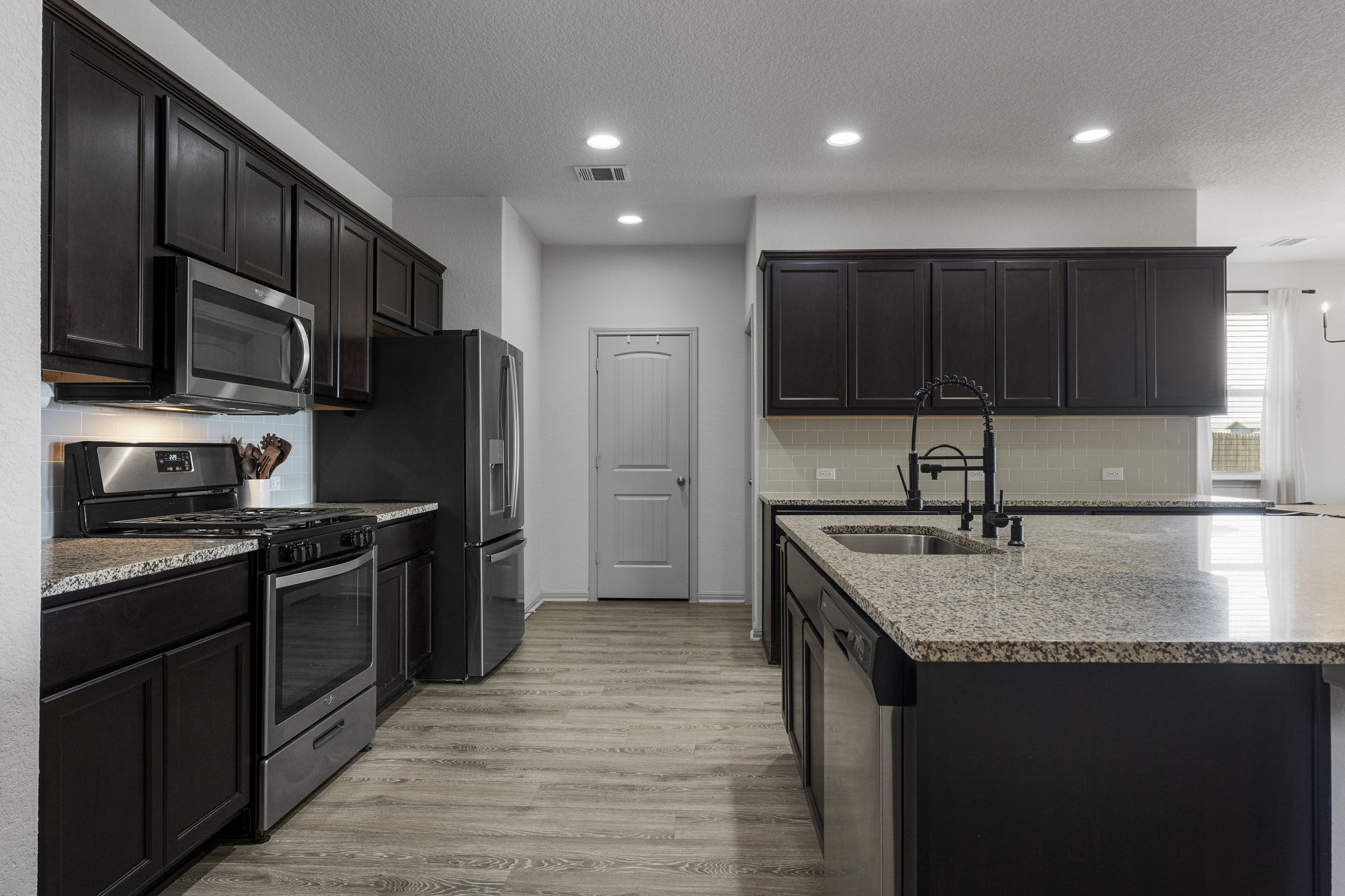 185 Struss Drive Georgetown, TX 78626 - Photo 5 of 23 A contemporary kitchen showcasing rich dark cabinetry, gleaming stone countertops, and sleek stainless steel appliances.
