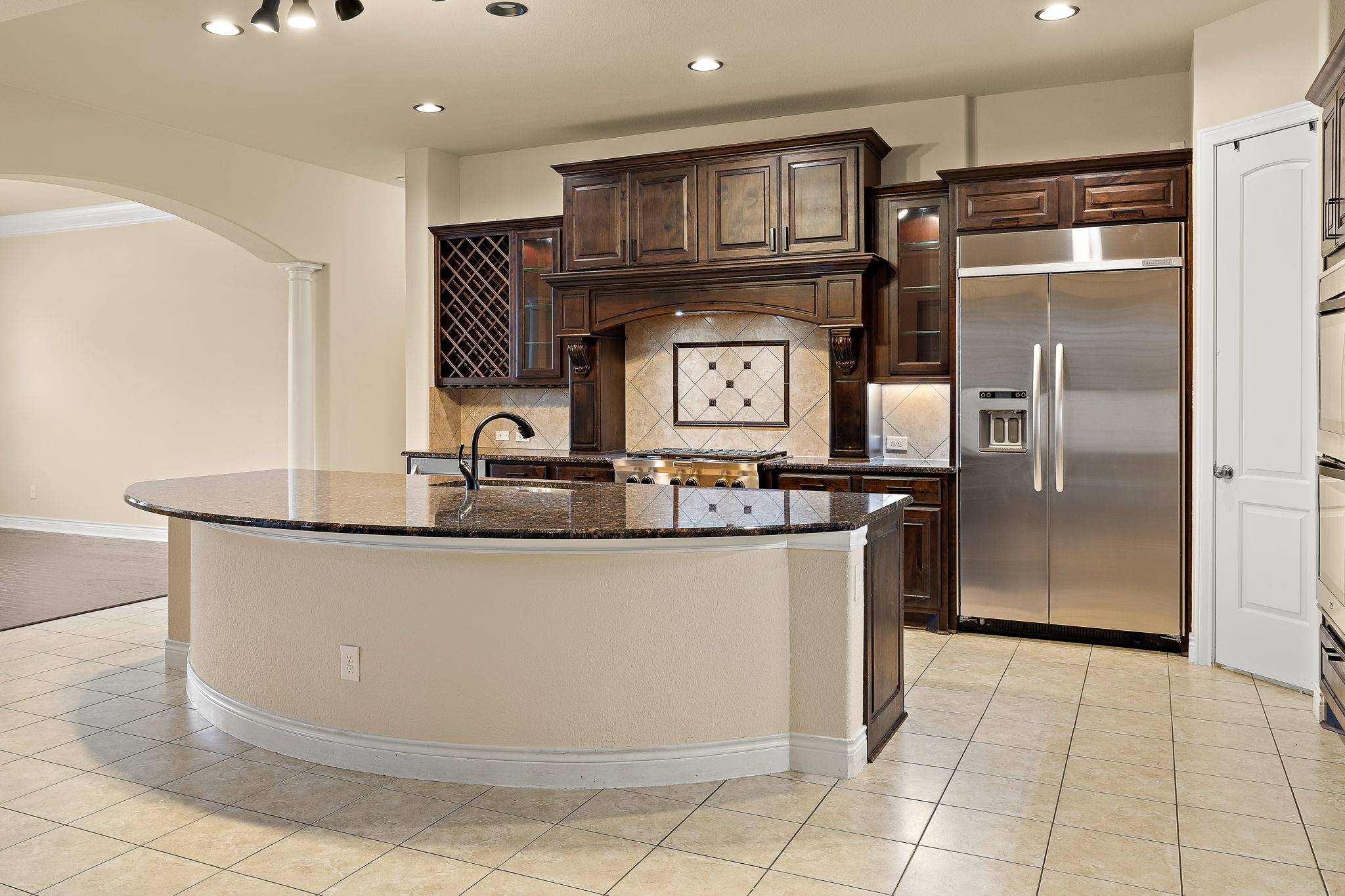 174 Estrella Crossing Georgetown, TX 78628 - Photo 10 of 38 Kitchen featuring glass insert cabinets, dark brown cabinetry, dark stone countertops, arched walkways, and stainless steel built in refrigerator
