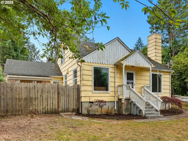 a view of a white house with a large tree and wooden fence
