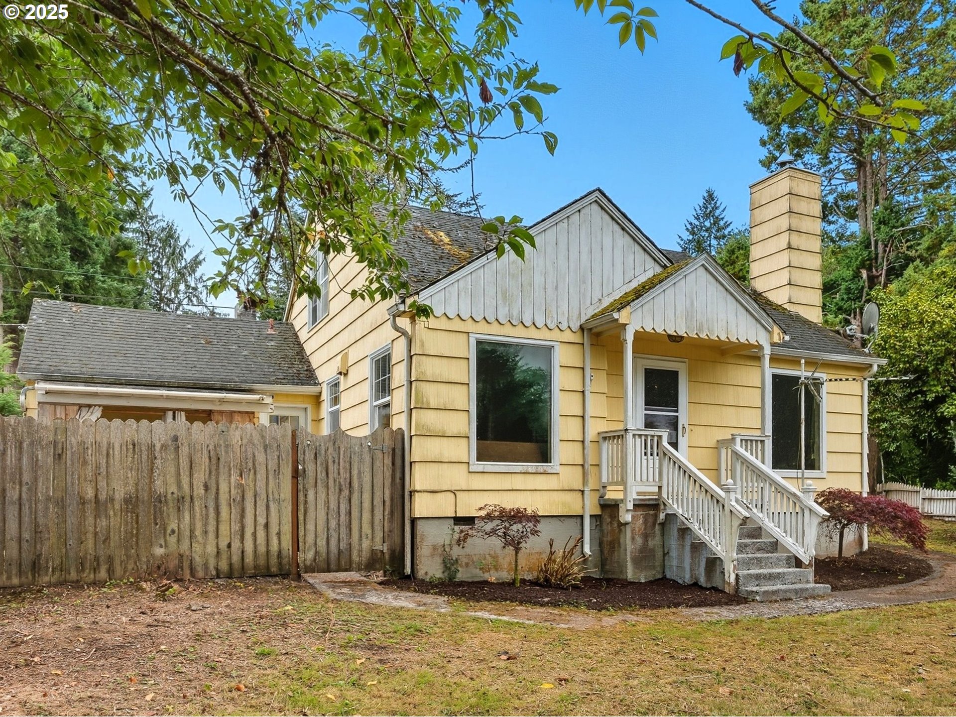 a view of a white house with a large tree and wooden fence