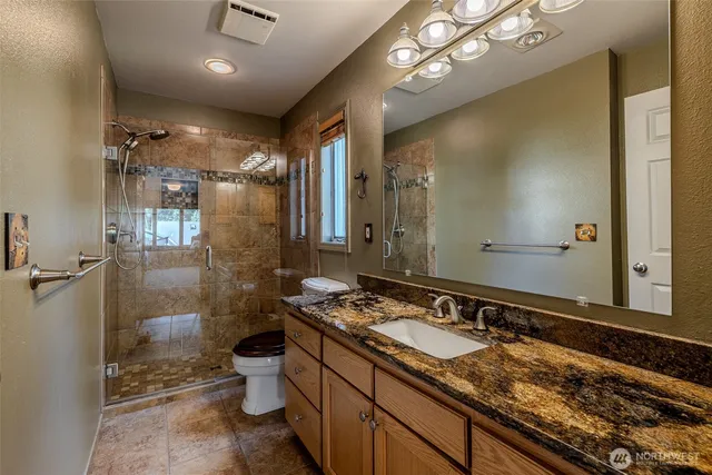 a bathroom with a granite countertop sink a toilet a mirror and shower