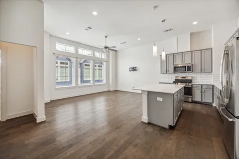 a large kitchen with stainless steel appliances granite countertop a stove a sink a refrigerator and white cabinets with wooden floor