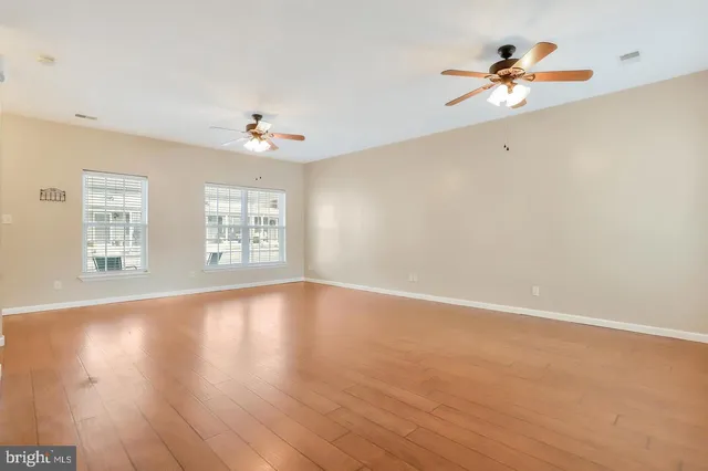 an empty room with wooden floor chandelier fan and windows