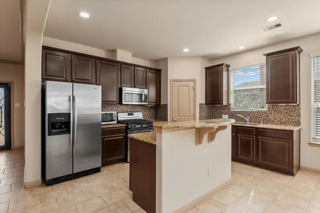 a kitchen with stainless steel appliances granite countertop a refrigerator a stove a sink a microwave and island