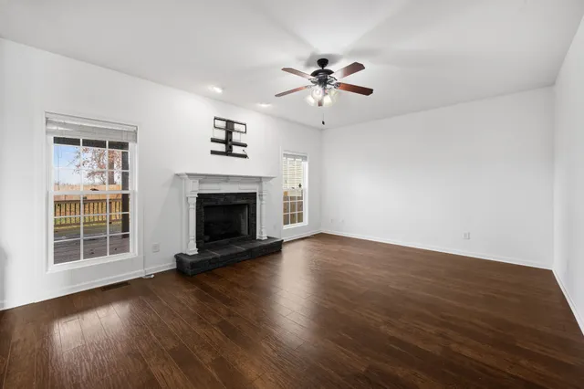 a view of an empty room with wooden floor fireplace and a window