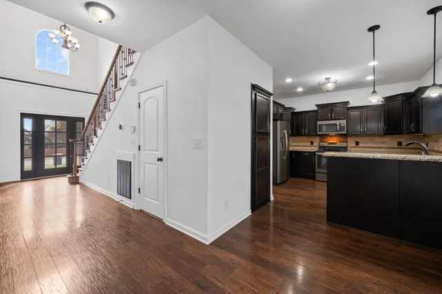 a view of kitchen with stainless steel appliances granite countertop a refrigerator a sink dishwasher a stove and a wooden floor