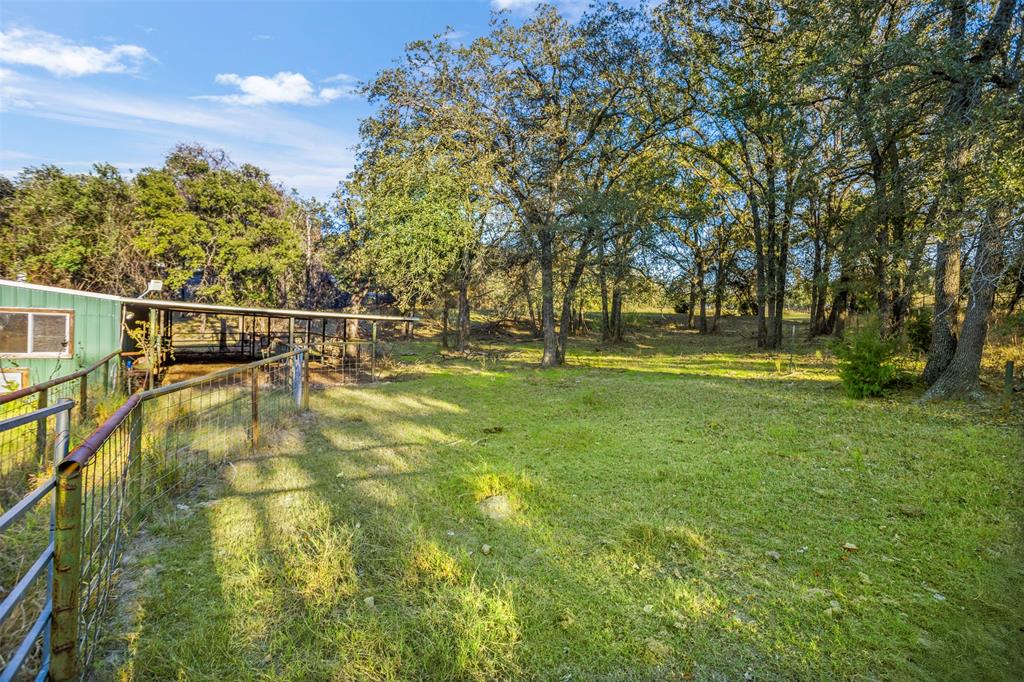 199 Cheyenne Trail Springtown, TX 76082 - Photo 4 of 22 Expansive greenspace featuring mature trees, a fenced enclosure, and a covered structure with an extended overhang