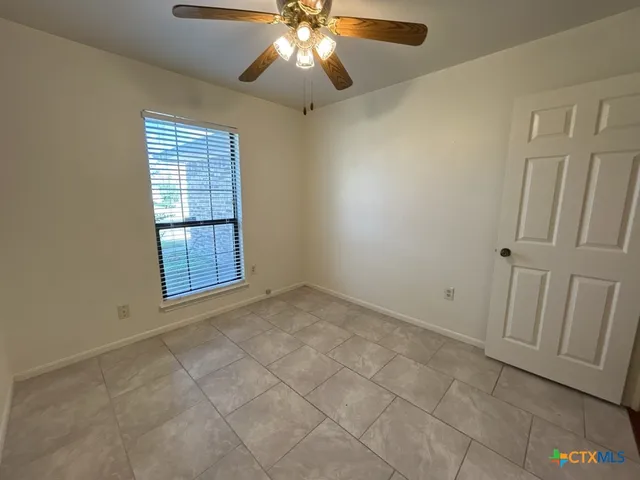 an empty room with chandelier fan and windows