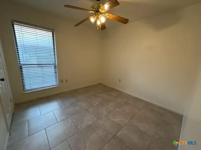 a view of an empty room with chandelier fan and a window
