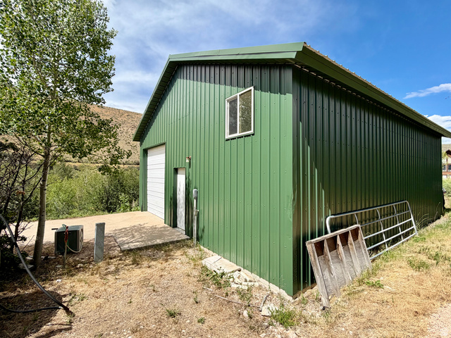 1133 Paris Canyon Road Paris, ID 83261 - Photo 40 of 75 Green corrugated metal pavilion featuring a white roll-up garage door, a single window, and a concrete pad