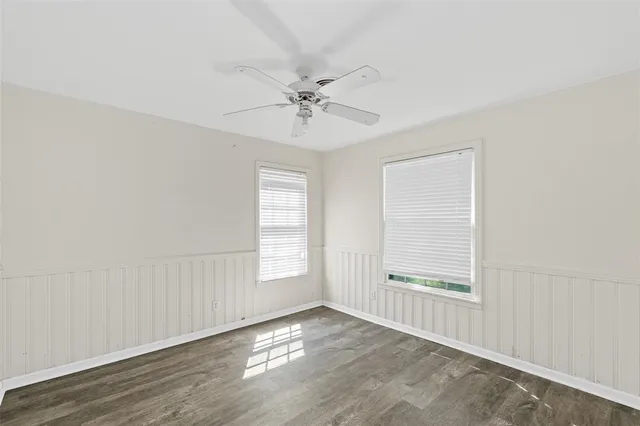 an empty room with wooden floor ceiling fan and windows