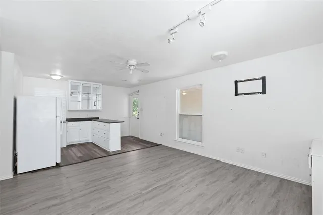 a view of an empty room with wooden floor and kitchen view