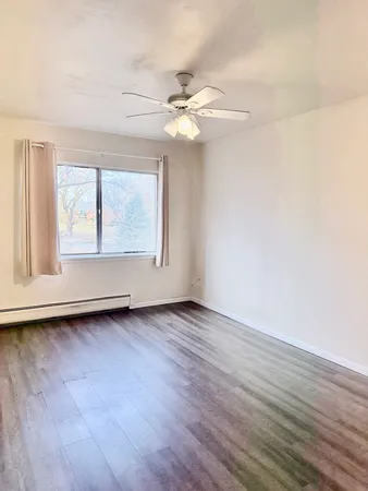 an empty room with wooden floor fan and windows