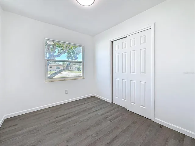 an empty room with wooden floor closet and windows
