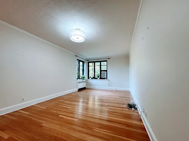 a view of an empty room with window and hardwood floor