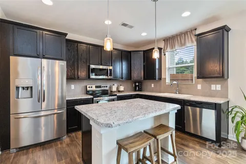 a kitchen with granite countertop a refrigerator a sink a stove a microwave and wooden floor