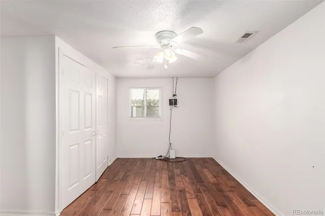 an empty room with wooden floor chandelier fan and windows
