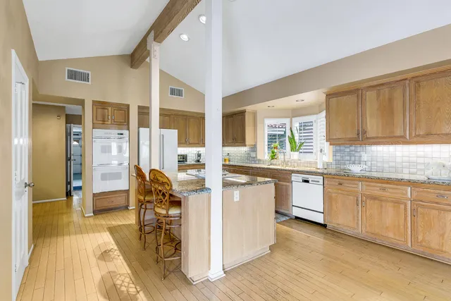 a kitchen with stainless steel appliances kitchen island granite countertop a refrigerator a oven a dining table and chairs with wooden floor