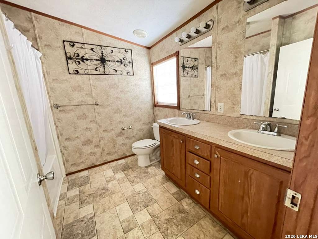 311 East Frio Street Dilley, TX 78017 - Photo 10 of 24 a bathroom with a granite countertop sink toilet a mirror a vanity and a shower