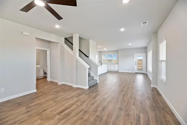 a view of an empty room with wooden floor ceiling fan