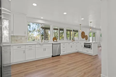 a large kitchen with stainless steel appliances kitchen island granite countertop a stove a sink and white cabinets with wooden floor