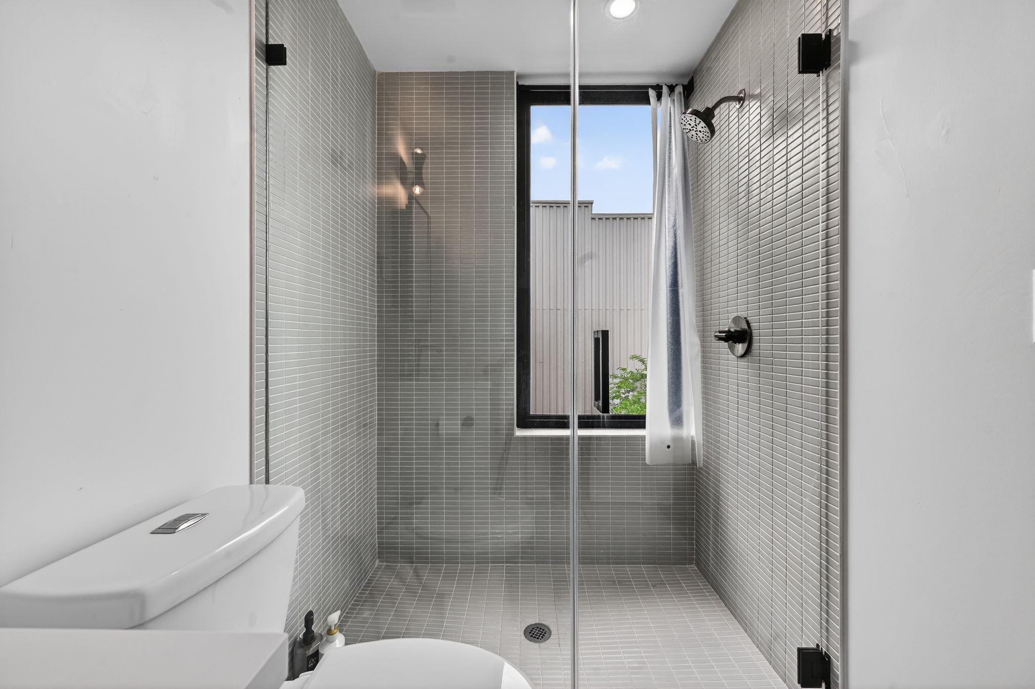 1206 Luna Street, Unit 2 Austin, TX 78721 - Photo 27 of 30 Bathroom featuring a shower with glass enclosure, light gray tiled walls and floor, and a window