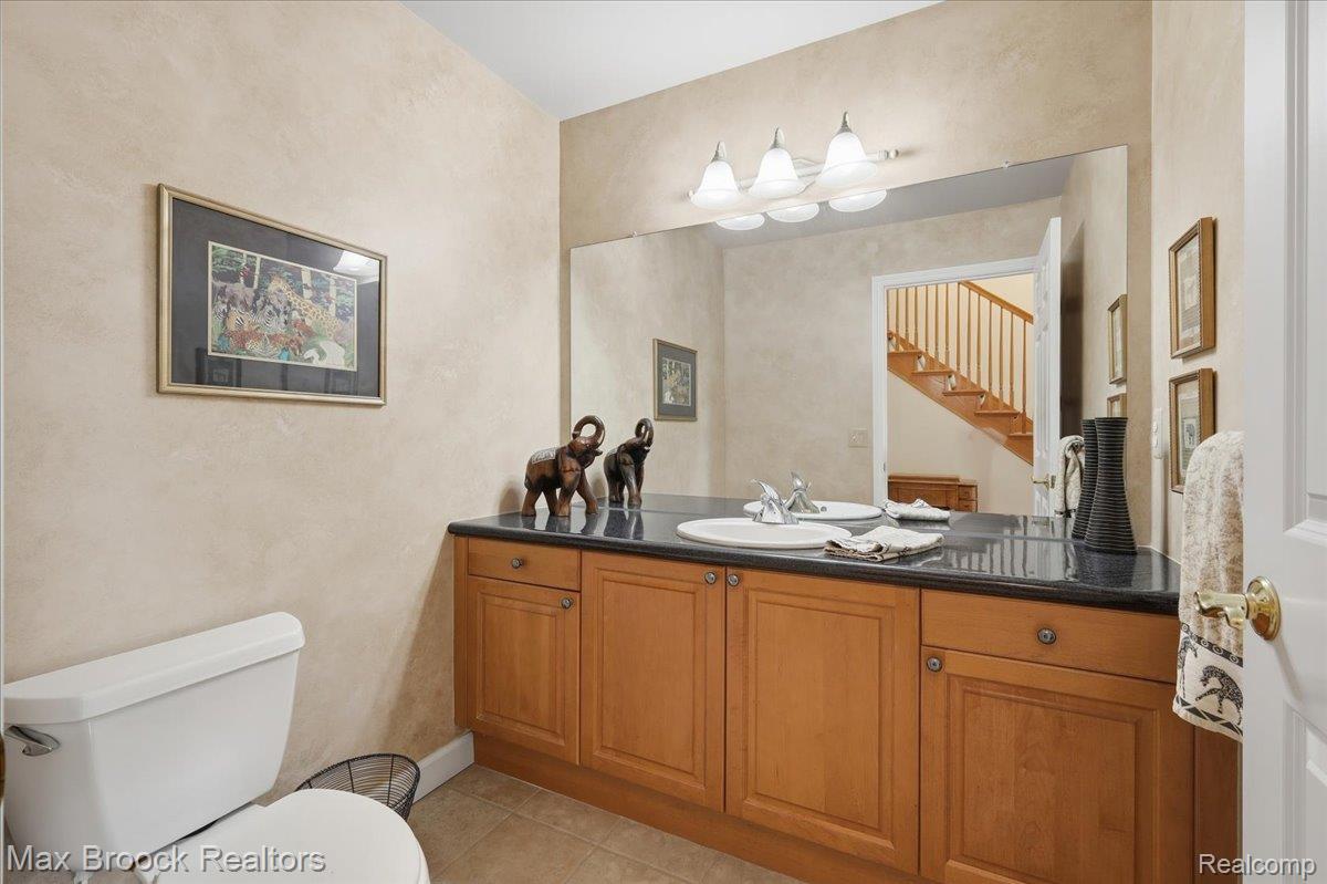 1731 Rico Road Commerce Township, MI 48382 - Photo 10 of 48 Double vanity with integrated sinks, black countertop, light wood cabinetry, and an expansive wall mirror