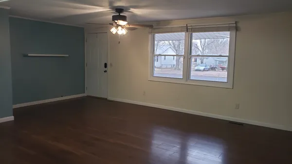an empty room with wooden floor chandelier fan and windows