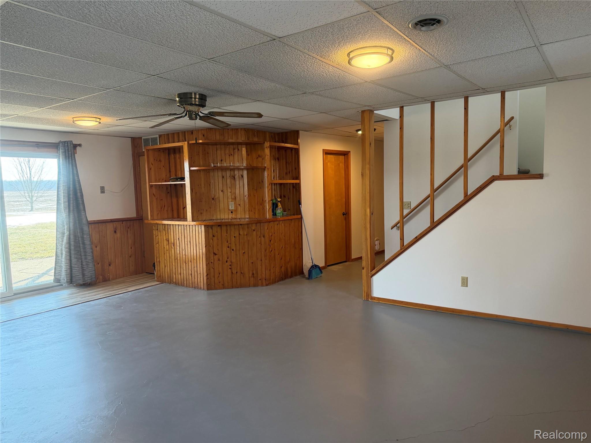 5749 Leix Road Mayville, MI 48744 - Photo 38 of 44 Unfurnished living room featuring wood walls, concrete flooring, ceiling fan, and wainscoting