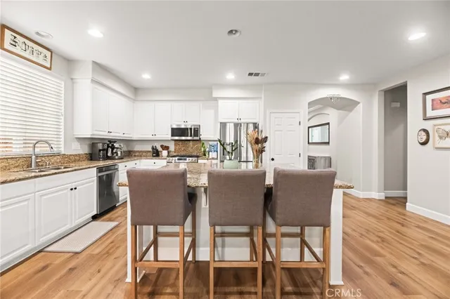 a large kitchen with stainless steel appliances kitchen island granite countertop a large kitchen island a stove a refrigerator a dining table and chairs with wooden floor