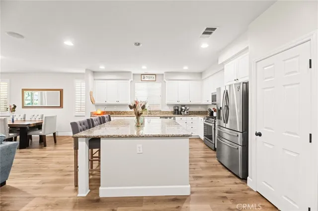 a kitchen with stainless steel appliances kitchen island granite countertop a stove a sink a refrigerator a dining table and chairs