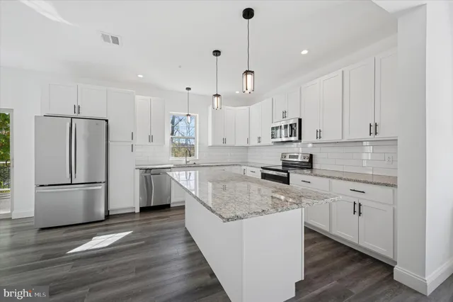 a kitchen with stainless steel appliances granite countertop a refrigerator a sink dishwasher a stove and white cabinets with wooden floor