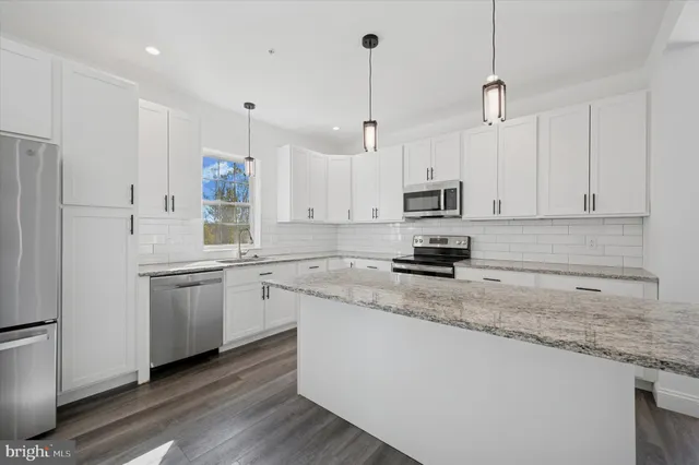 a kitchen with stainless steel appliances granite countertop a sink a stove a refrigerator and white cabinets