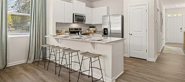 a kitchen with stainless steel appliances granite countertop a refrigerator a stove a sink and white cabinets with wooden floor