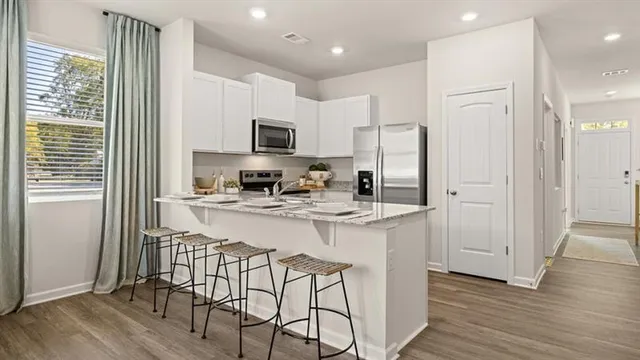 a kitchen with stainless steel appliances granite countertop a refrigerator a stove a sink and white cabinets with wooden floor