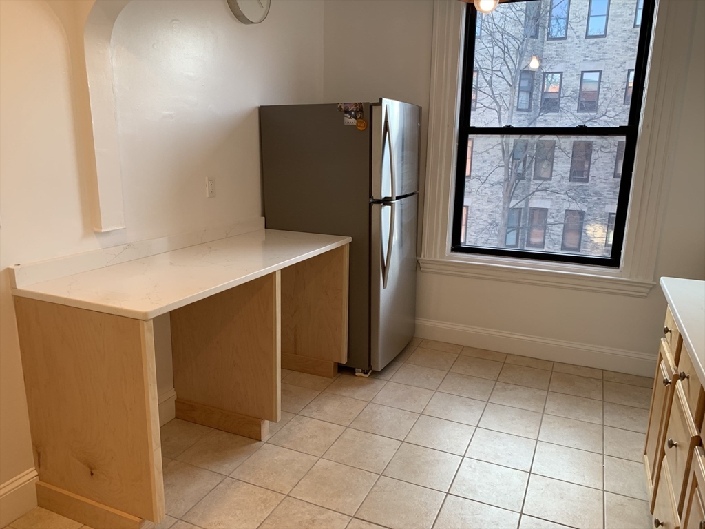 1064 Beacon Street, Unit 9 Brookline, MA 02446 - Photo 6 of 19 a view of a refrigerator in kitchen and an empty room with wooden floor