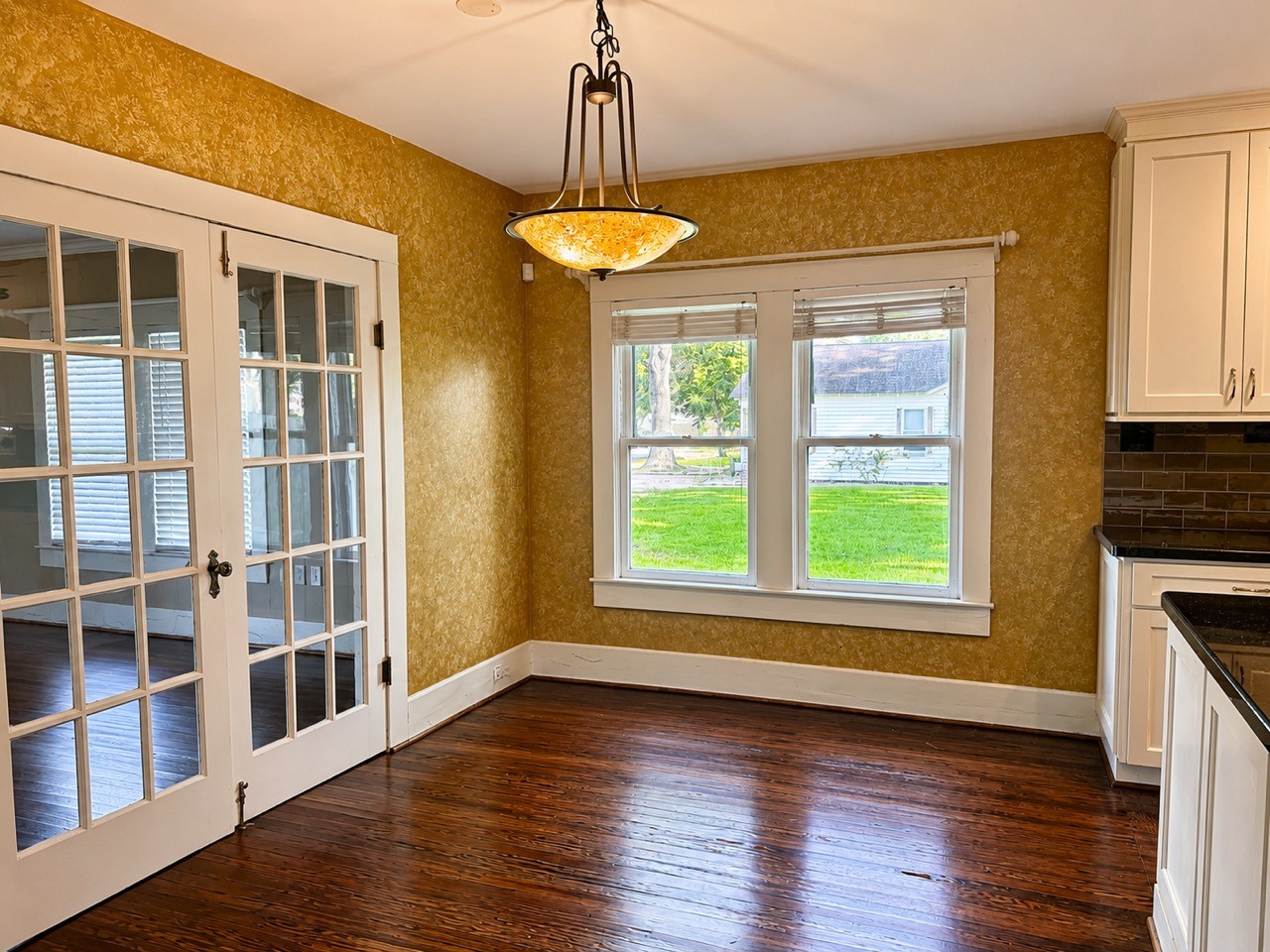 1726 7th Street Rosenberg, TX 77471 - Photo 4 of 17 Bright dining area with warm-toned walls and rich hardwood floors. Features large windows for natural light, French doors, and a classic chandelier.