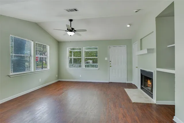 a view of an empty room with wooden floor fireplace and a window