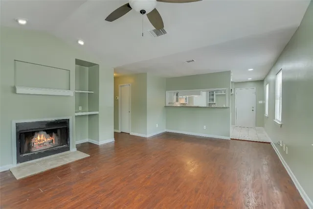 a view of an empty room with wooden floor fireplace and a window