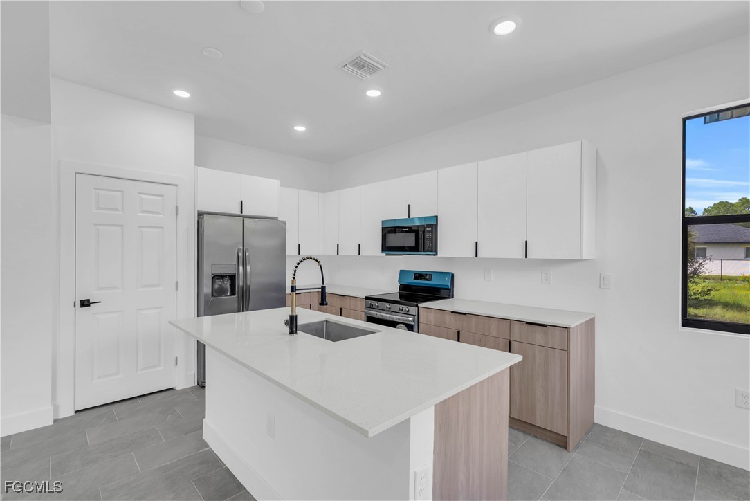 3224 53rd Street West Lehigh Acres, FL 33971 - Photo 6 of 22 a kitchen with stainless steel appliances a sink a refrigerator and white cabinets