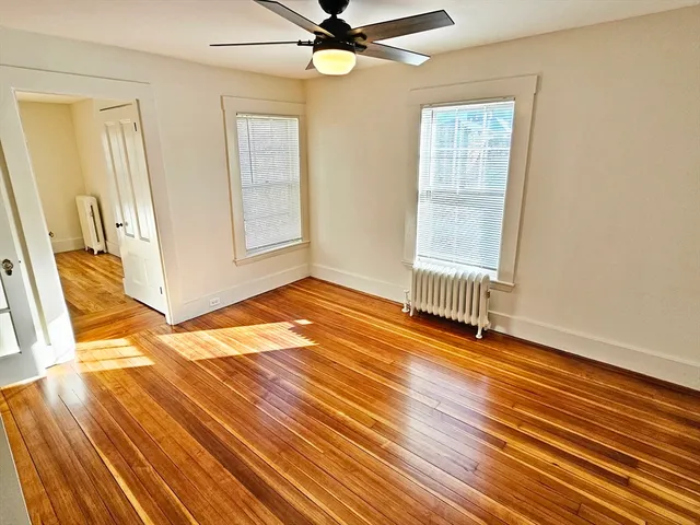 an empty room with wooden floor fan and windows