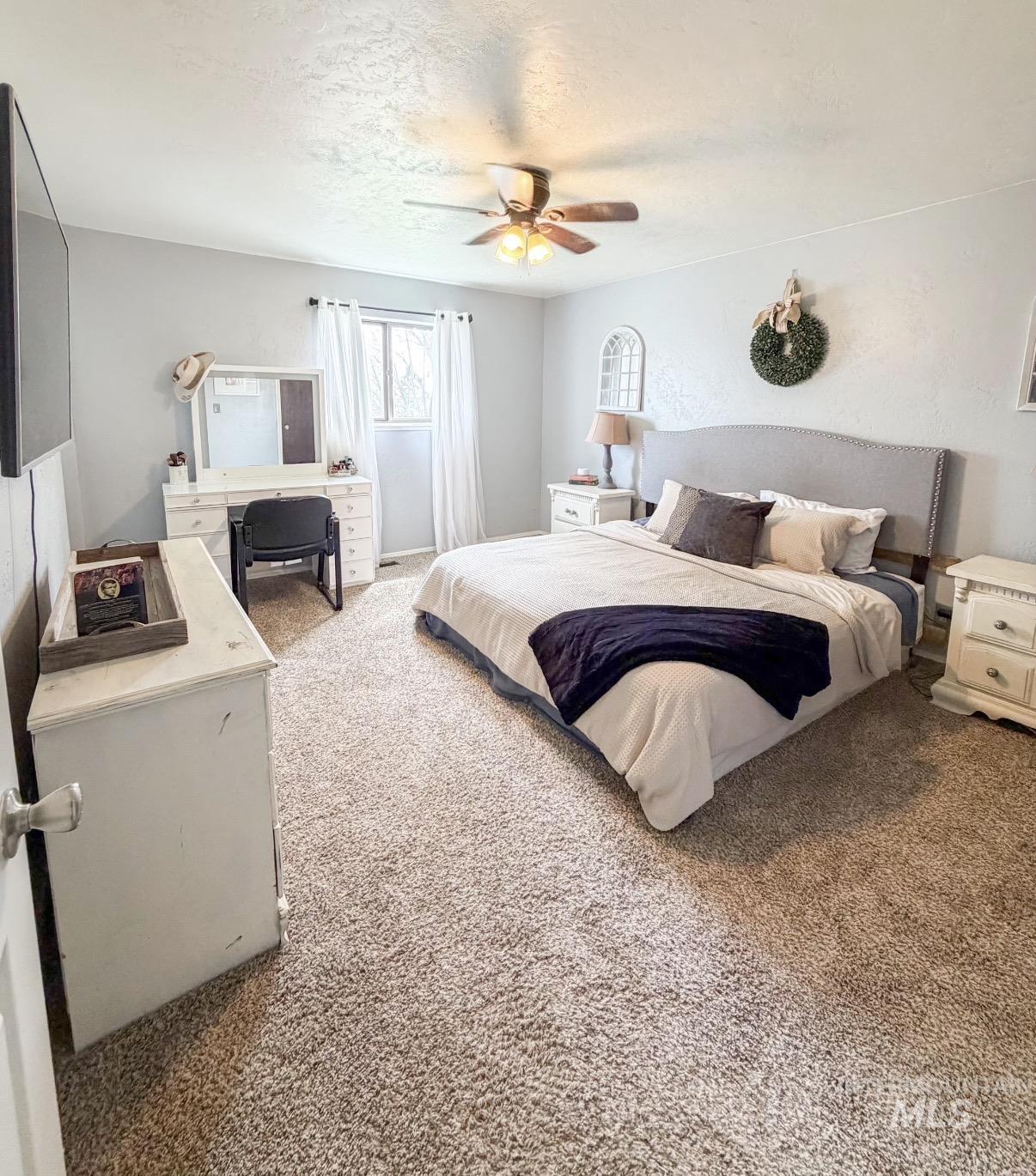 1452 Weiser River Road Weiser, ID 83672 - Photo 22 of 38 Carpeted bedroom featuring a window with white drapes, a ceiling fan with integrated lighting, and light gray wall paint