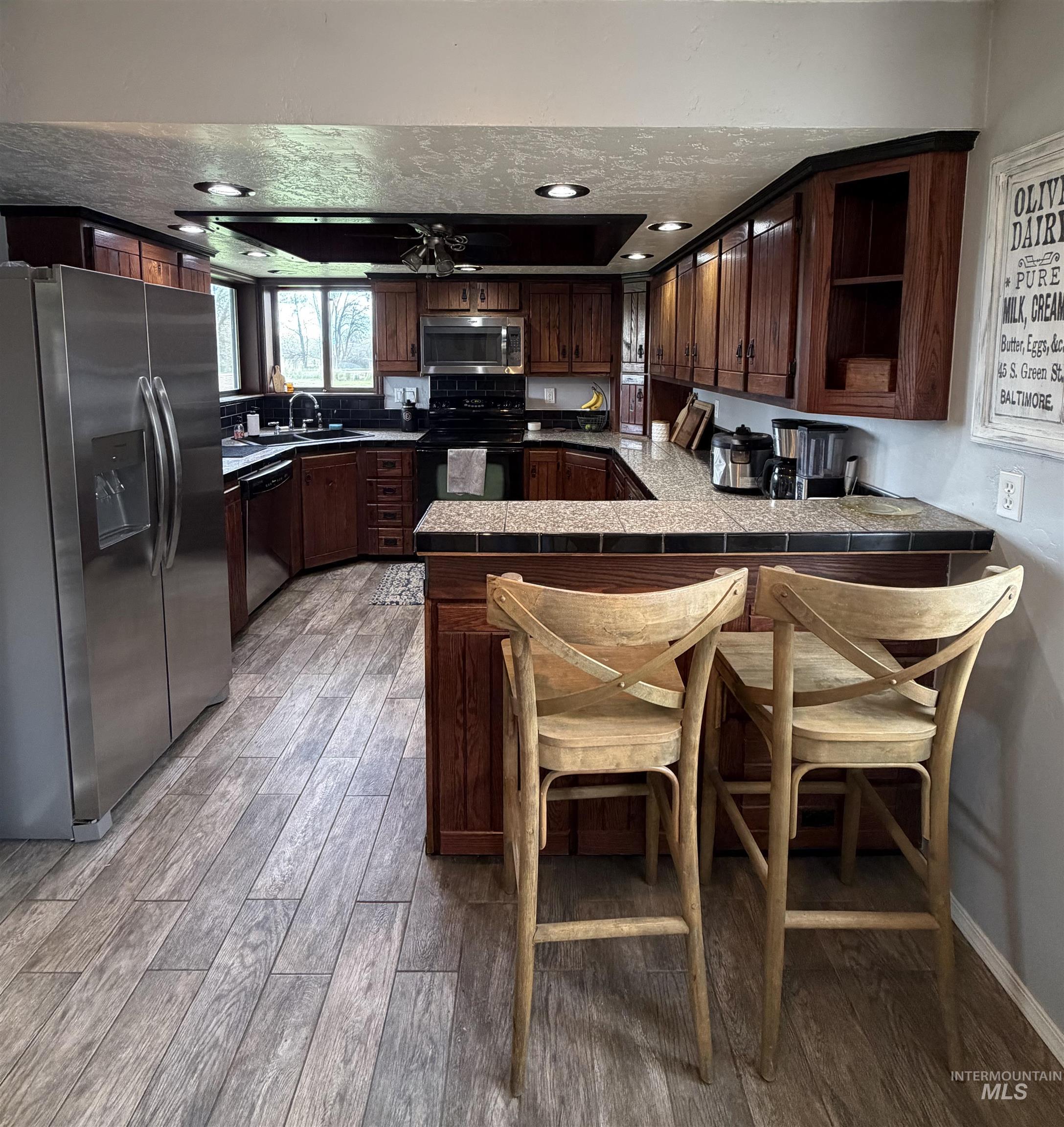 1452 Weiser River Road Weiser, ID 83672 - Photo 8 of 40 Kitchen with stainless steel appliances, a peninsula, a tray ceiling, tile counters, and dark wood finish cabinets