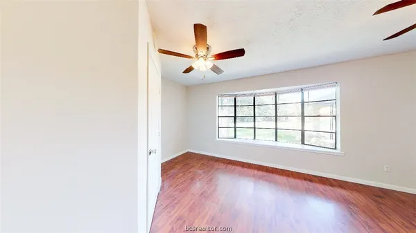 an empty room with wooden floor fan and windows
