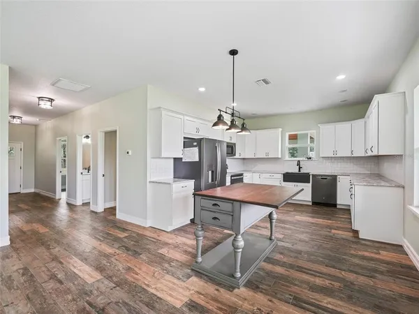 a room with stainless steel appliances kitchen island granite countertop a refrigerator a stove a sink dishwasher and white cabinets with wooden floor