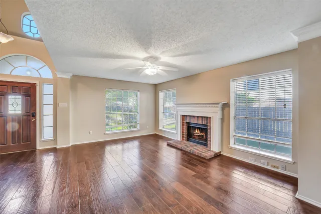 a view of a livingroom with wooden floor a fireplace a ceiling fan and windows