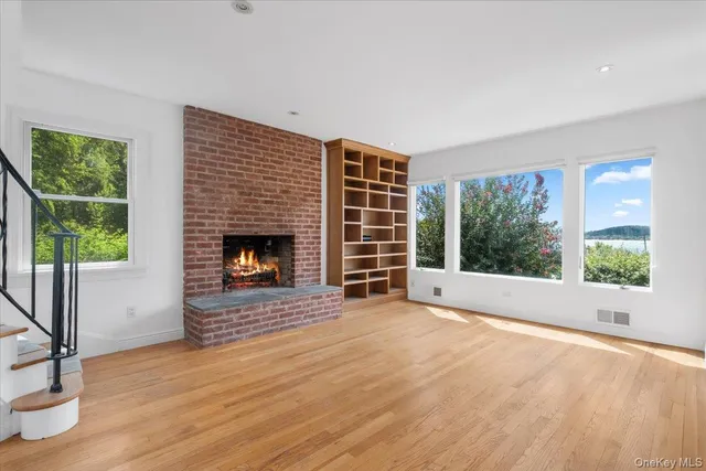 a view of an empty room with wooden floor fireplace and a window