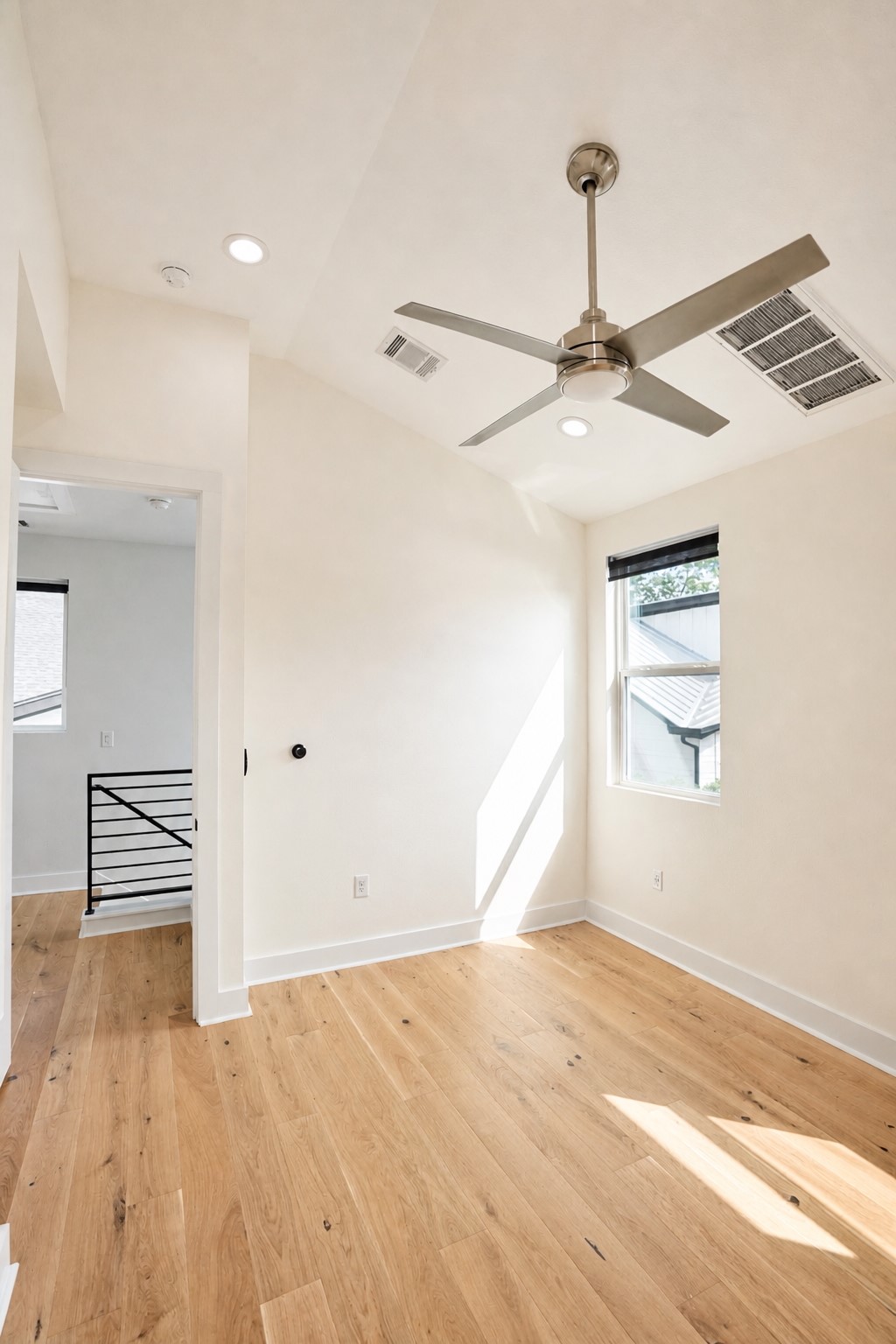1123 Omega Avenue, Unit 1 Austin, TX 78721 - Photo 15 of 40 Spacious room featuring wood-finish flooring, a contemporary ceiling fan, recessed lighting, a single window with a dark roller shade, and white walls with crisp baseboards