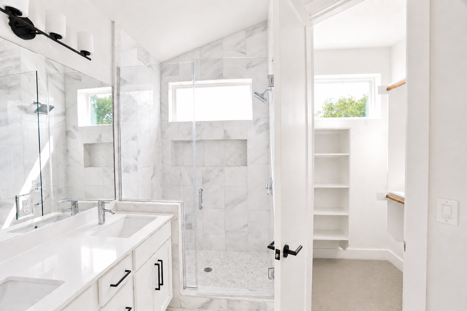 1123 Omega Avenue, Unit 1 Austin, TX 78721 - Photo 18 of 40 Modern bathroom featuring a dual vanity with white countertops, a walk-in shower with glass enclosure, white marble-style wall tiling, and an adjacent walk-in closet with built-in shelving