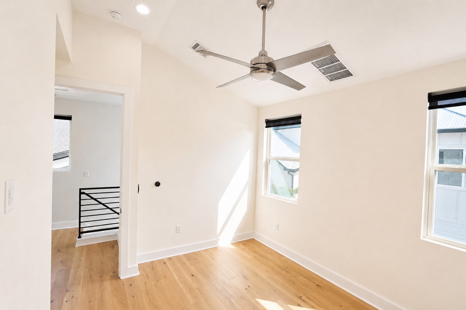 1123 Omega Avenue, Unit 1 Austin, TX 78721 - Photo 24 of 40 Room with wood-finish flooring, two windows with dark roller shades, and a ceiling fan with brushed nickel finish